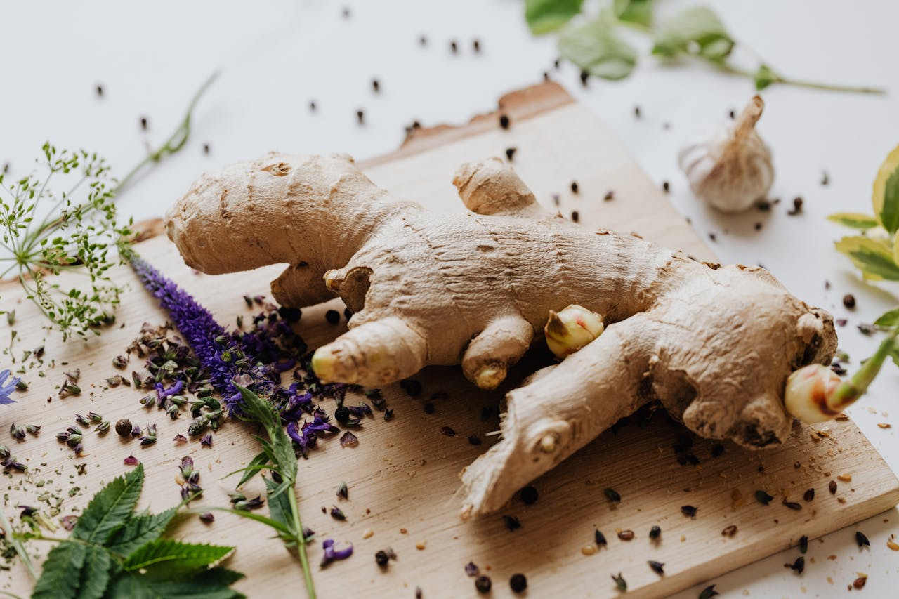 Close-up of fresh ginger root surrounded by spices and herbs on a wooden chopping board.