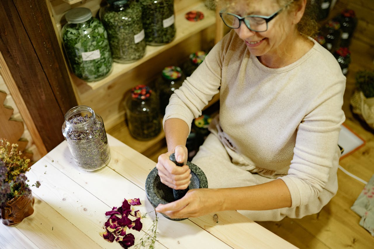 Woman smiling while grinding herbs using a mortar and pestle in a cozy home setting.